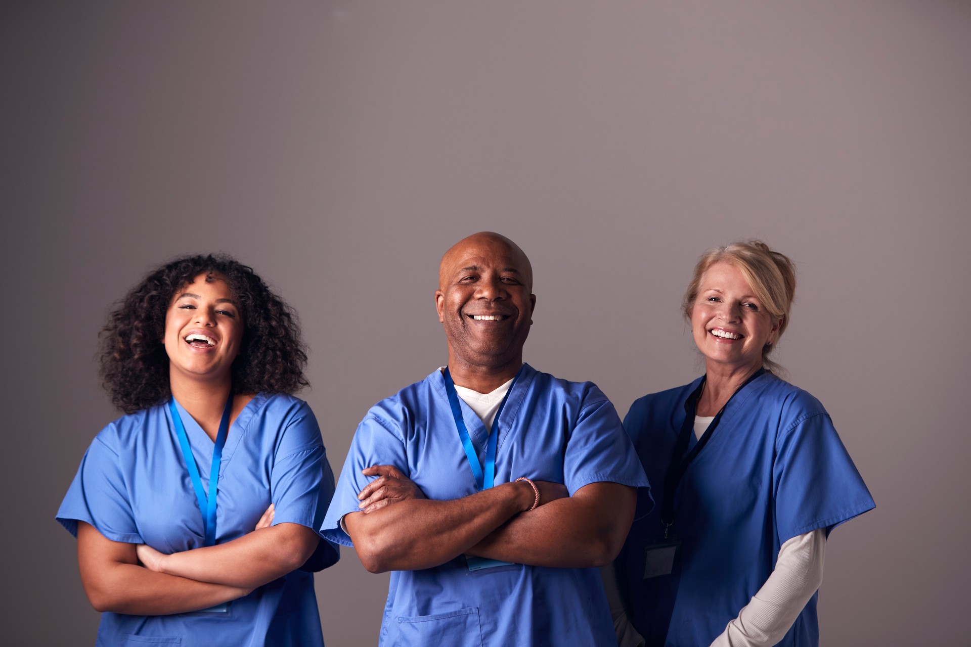 Studio Portrait Of Three Members Of Surgical Team Wearing Scrubs Standing Against Grey Background Studio Portrait Of Three Members Of Surgical Team Wearing Scrubs Standing Against Grey Background